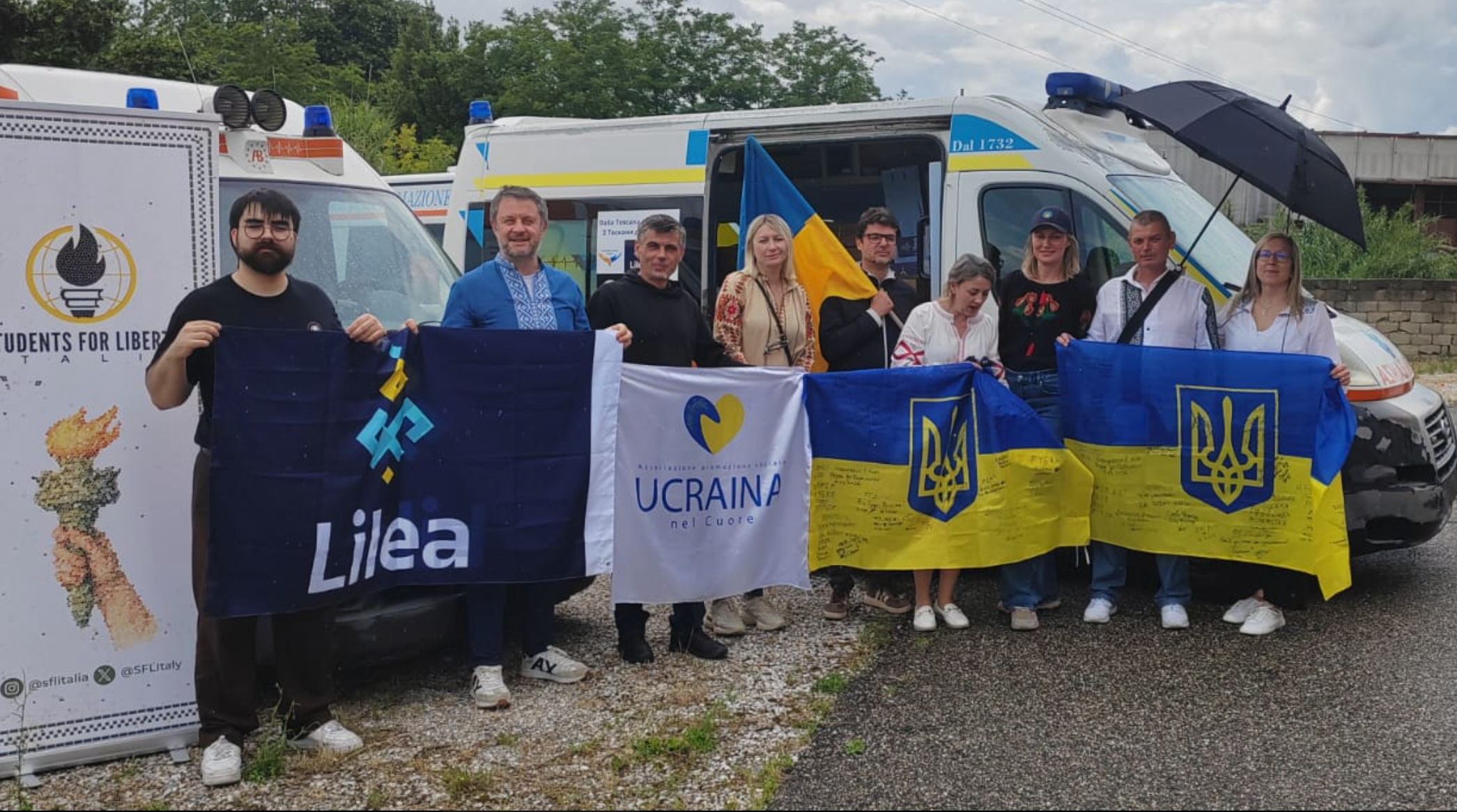 Lilea volunteers and friends posing in front of two donated ambulances, with flags of Ukraine and of pro-Ukrainian associations