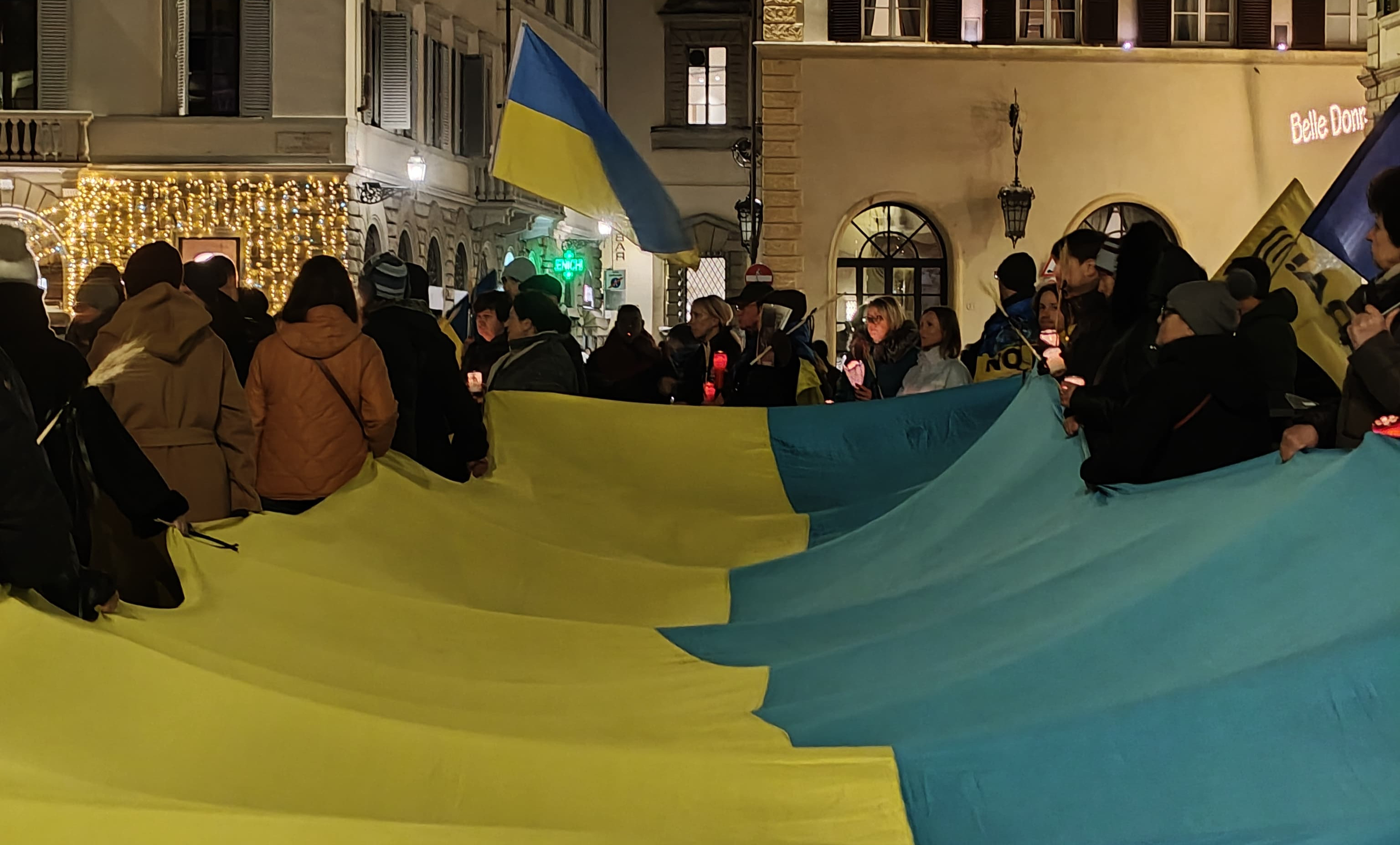 A very big Ukrainian flag being held by a lot of people in a rally in Florence